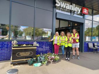 Four adults standing in from of Swanley station next to the flowers they planted in a trough.